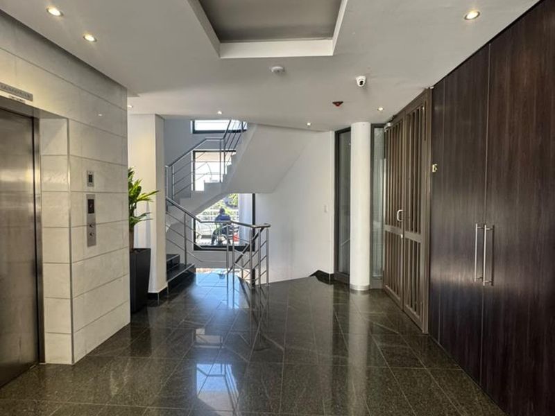 Modern office building entrance lobby featuring polished tile flooring, a stainless steel elevator, built-in storage cabinetry, and a central staircase.