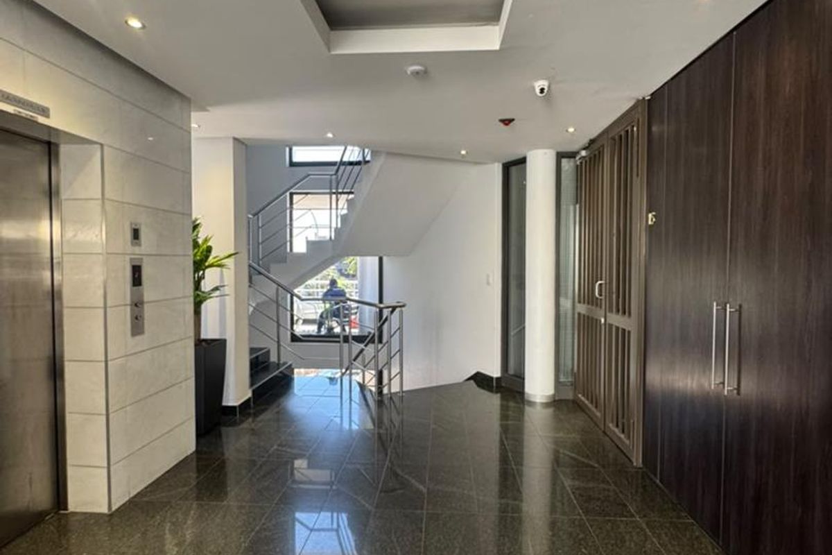 Modern office building entrance lobby featuring polished tile flooring, a stainless steel elevator, built-in storage cabinetry, and a central staircase.