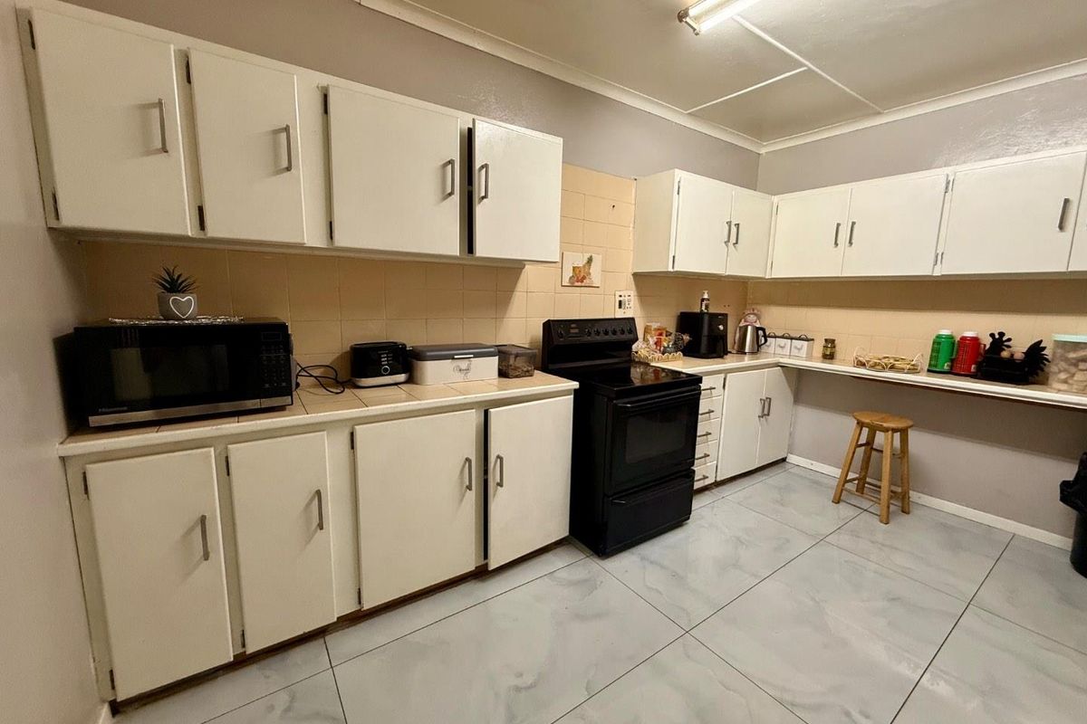 Functional kitchen featuring white cabinetry, tiled backsplash, and a freestanding stove, finished with modern floor tiles.