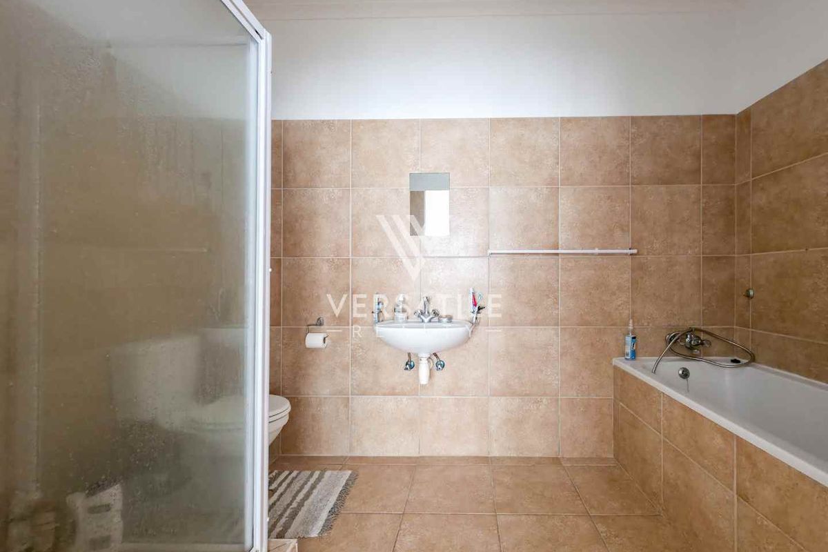 A functional bathroom featuring a built-in bathtub, a separate glass-enclosed shower, and wall-mounted basin with neutral floor-to-ceiling tiling.