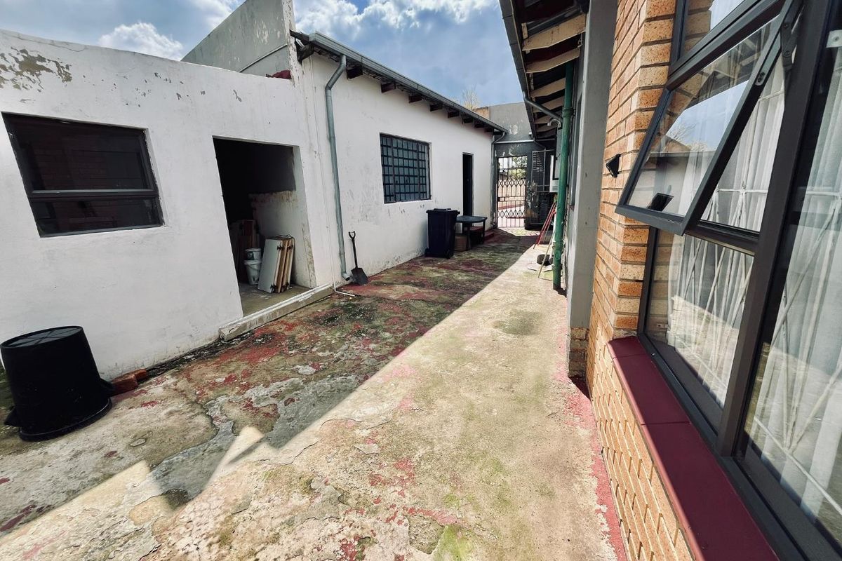 A narrow exterior side passage featuring weathered concrete paving and exposed brickwork, providing access to the rear of the property.