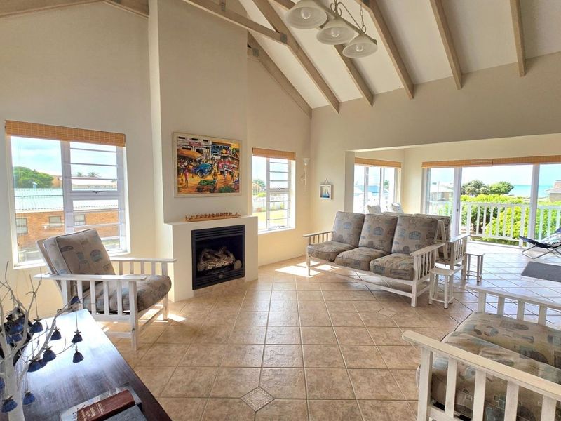 Spacious living room featuring a high vaulted ceiling with exposed beams, a built-in fireplace, tiled flooring, and large windows with access to a balcony.