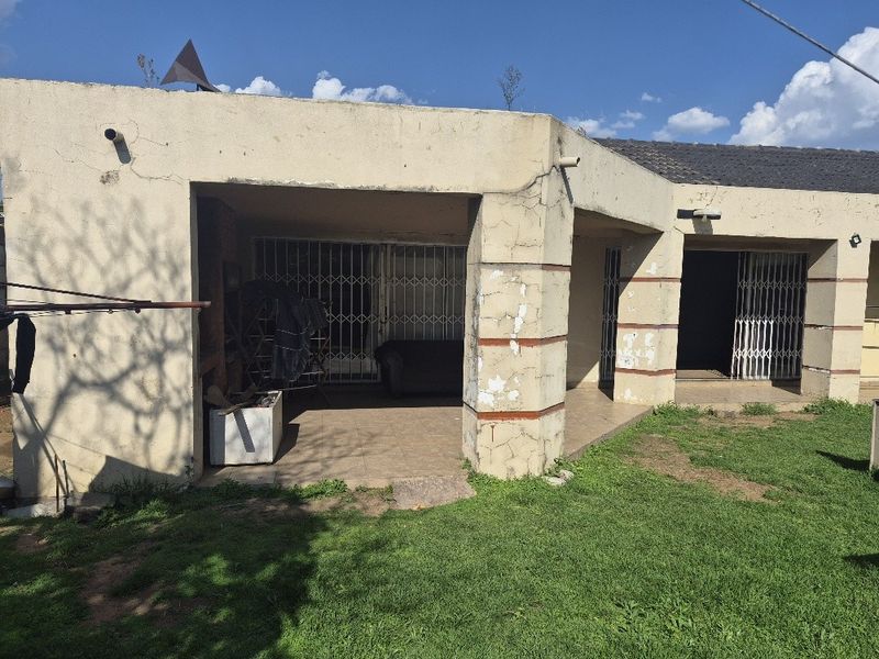 Rear view of the property featuring a covered patio area with security gates and visible wear to the exterior plaster and paint finishes.
