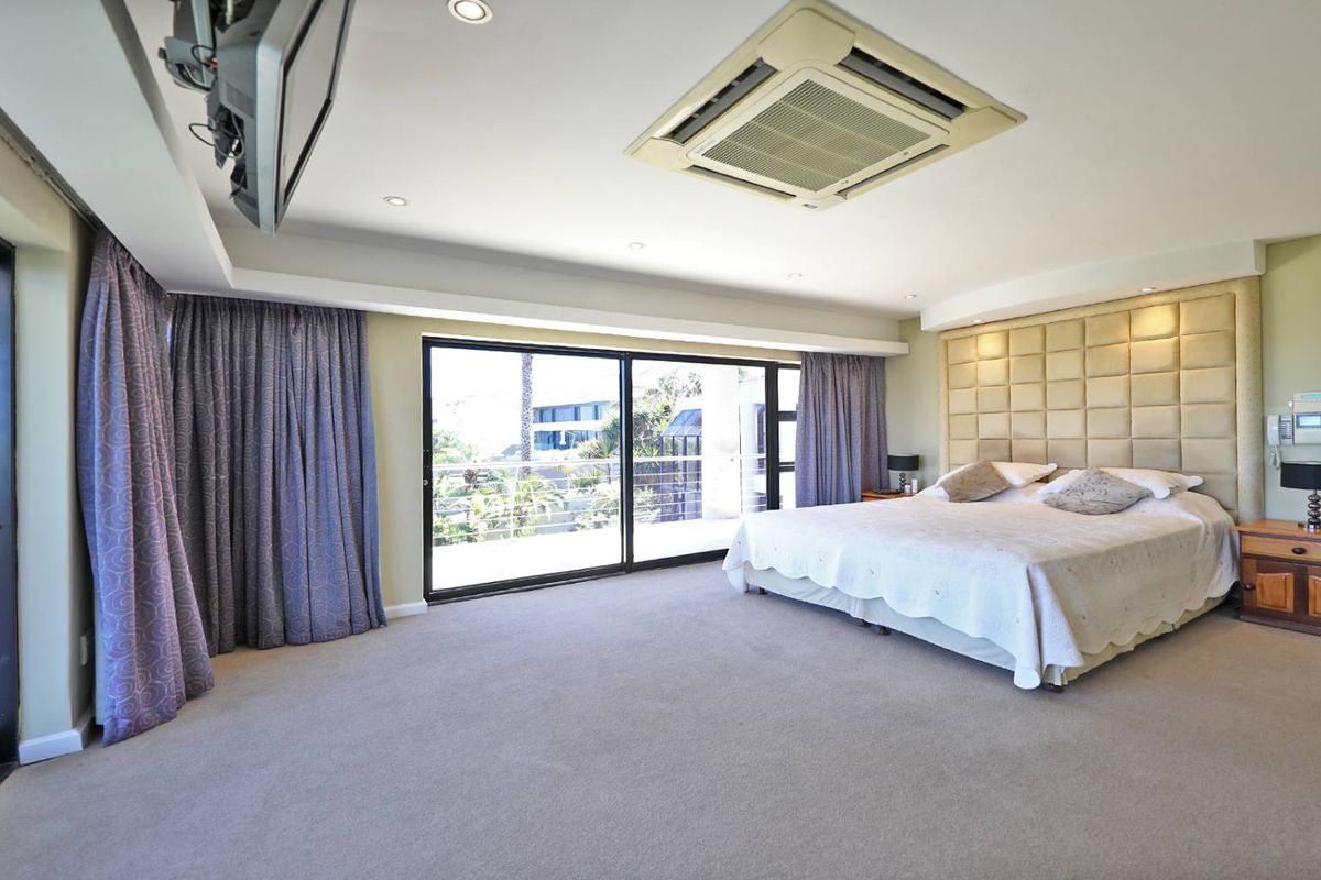 Spacious bedroom featuring a large upholstered headboard, recessed ceiling lighting, integrated air conditioning unit, and expansive sliding glass doors leading to a private balcony.