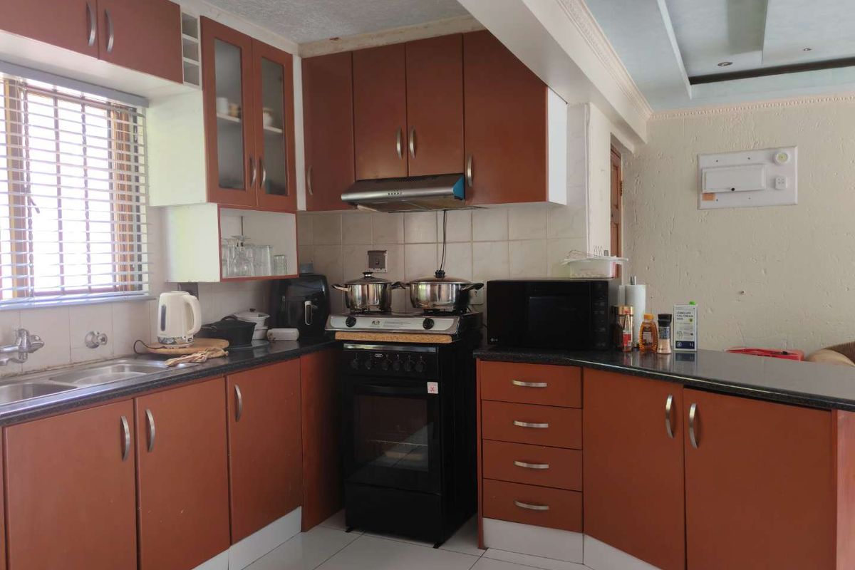 A functional kitchen featuring laminate cabinetry, granite countertops, a tiled backsplash, and a freestanding oven with an extractor fan.