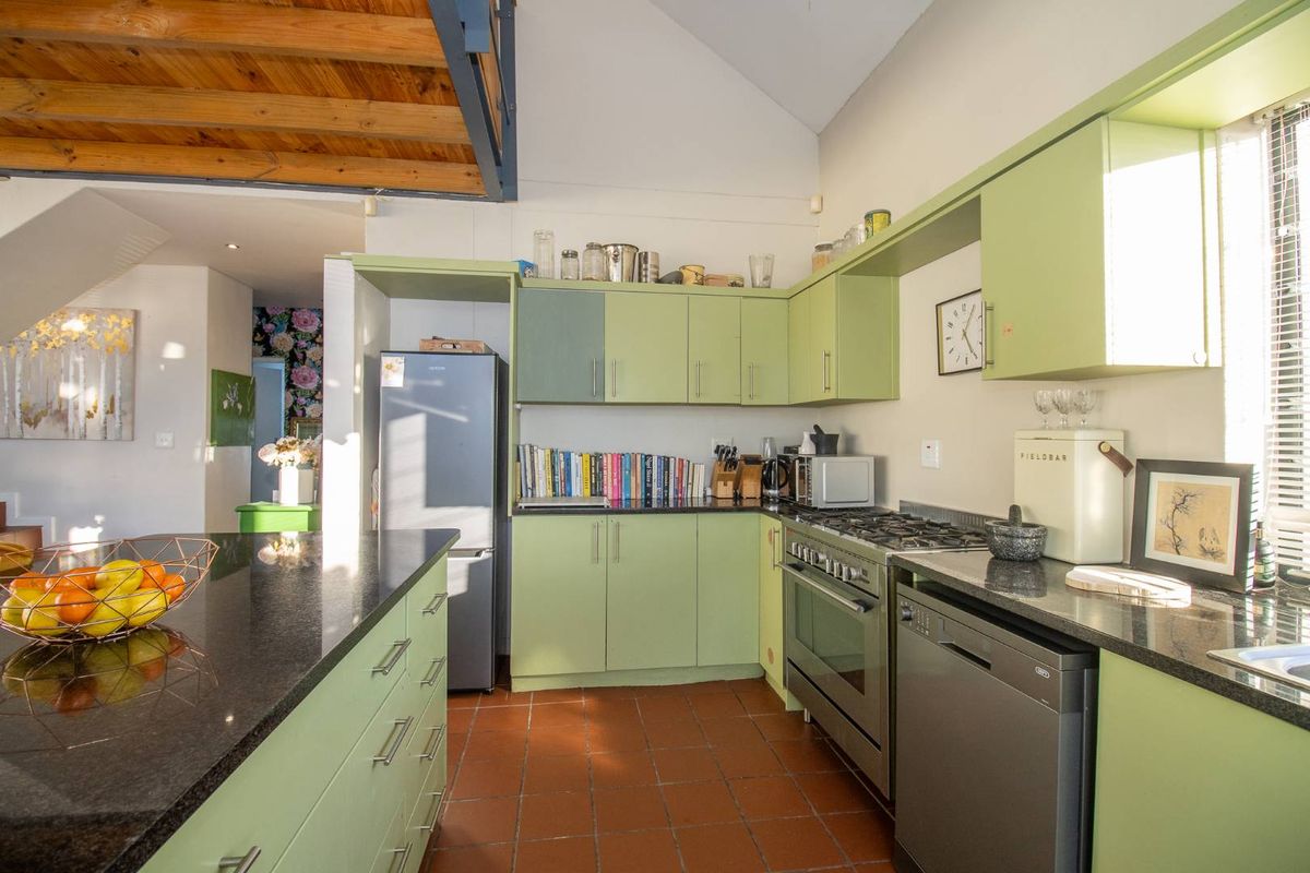 A functional kitchen featuring light green cabinetry, dark granite countertops, a gas stove, and terracotta floor tiles, with an open-plan layout.