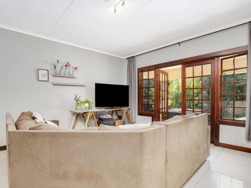 A bright living room featuring tiled flooring and wooden framed glass french doors that provide direct access to the outdoor area.