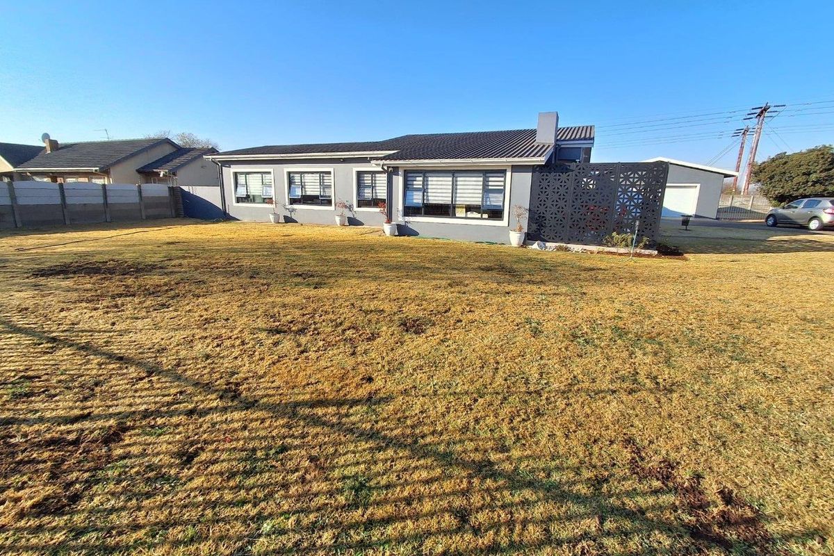 Rear view of the house featuring a large lawn, metal roof, and decorative privacy screen, set within a fenced property boundary.