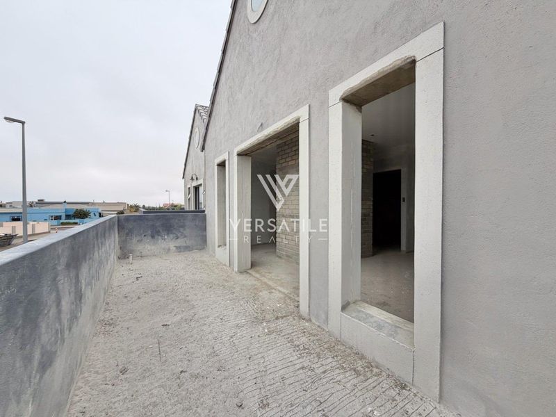 An unfinished balcony area featuring concrete flooring and stone-trimmed door openings, awaiting final finishes and installation of doors.