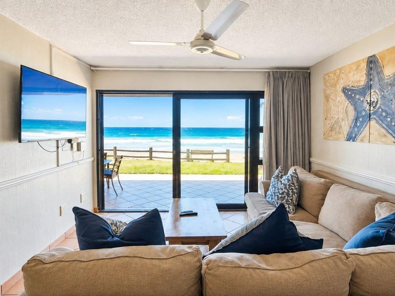 Comfortable living room featuring tiled flooring, a ceiling fan, and large sliding glass doors that open to a scenic ocean view.
