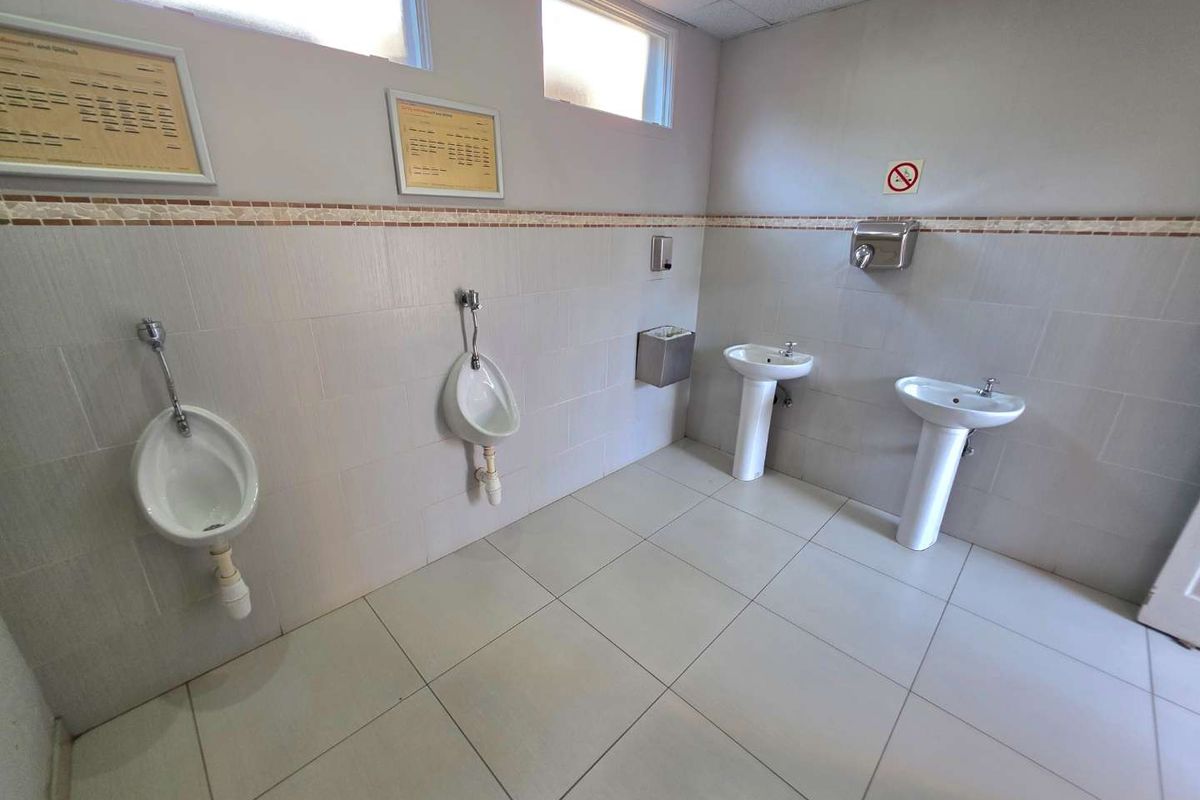 A functional commercial restroom facility featuring wall-mounted urinals, pedestal wash basins, and tiled finishes throughout.