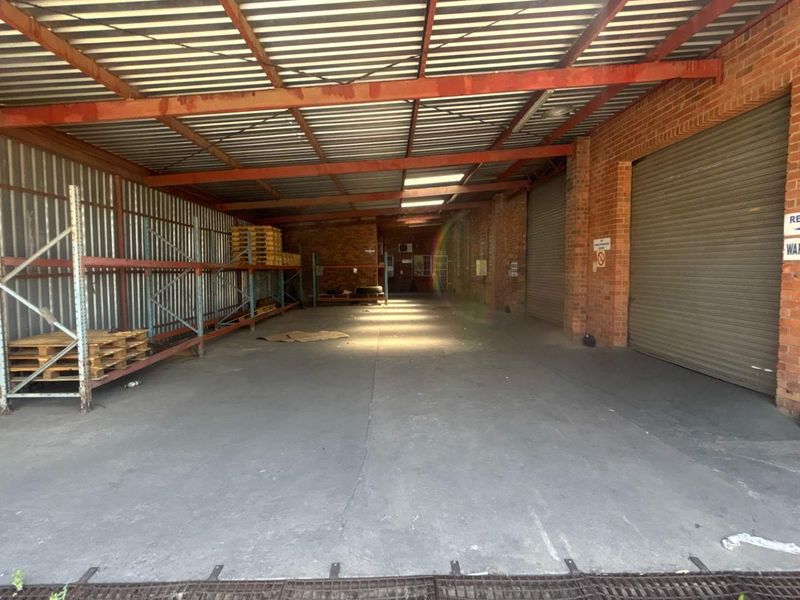 Spacious industrial utility area featuring concrete flooring, exposed brick walls, steel roof trusses, and roller shutter doors, suitable for storage or workshop use.