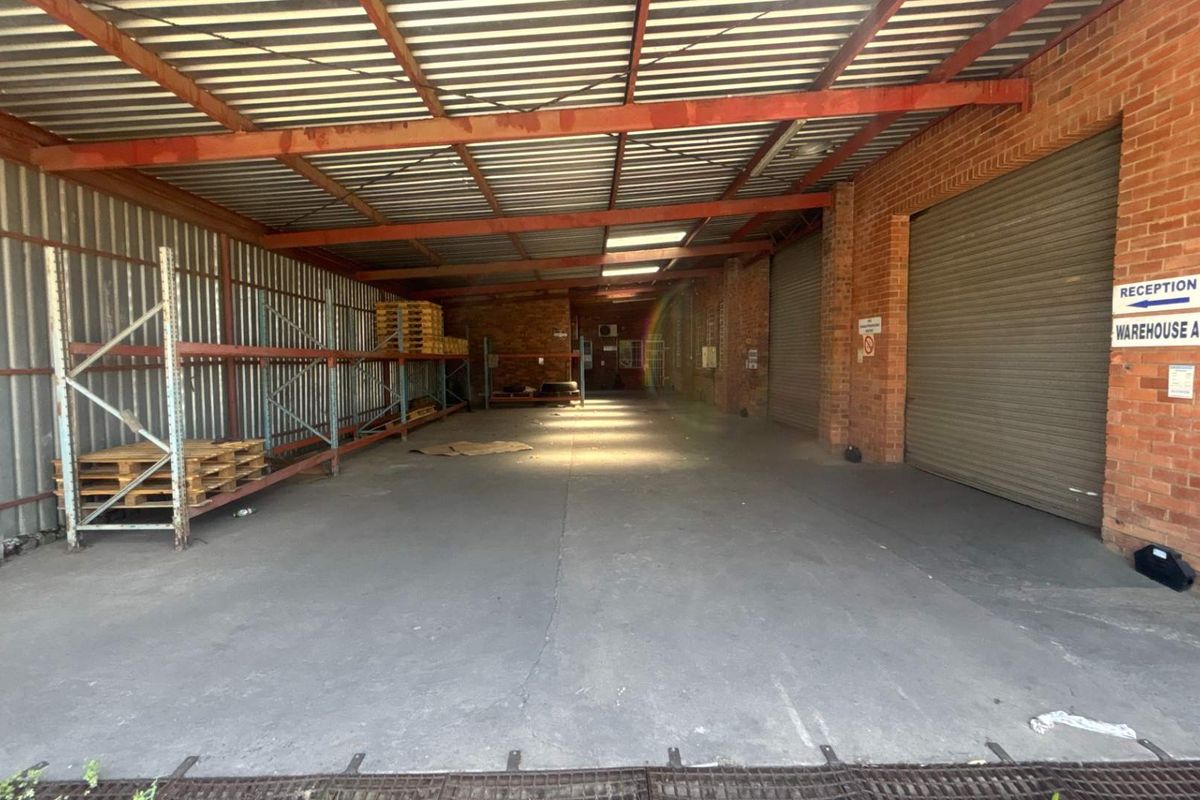 Spacious industrial utility area featuring concrete flooring, exposed brick walls, steel roof trusses, and roller shutter doors, suitable for storage or workshop use.
