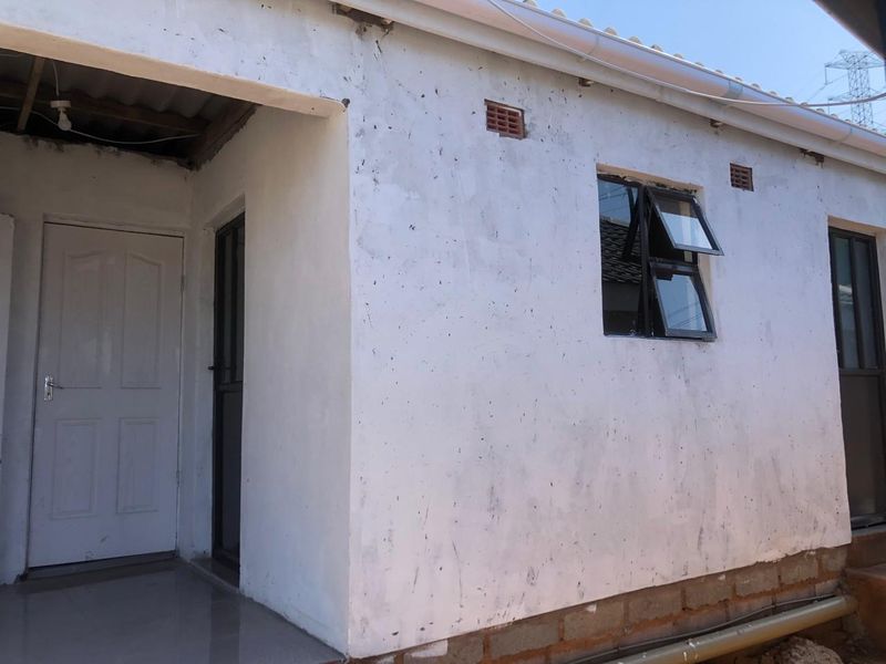 Rear exterior view of the cottage showing white rendered walls, aluminium window frames, and an unfinished base section.