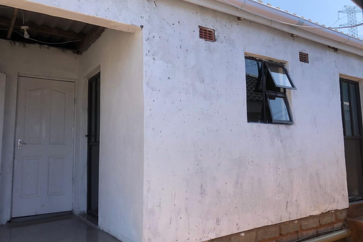 Rear exterior view of the cottage showing white rendered walls, aluminium window frames, and an unfinished base section.