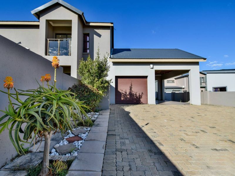 Front view of a modern double-story house featuring a paved driveway, integrated garage, and a balcony with glass balustrades.