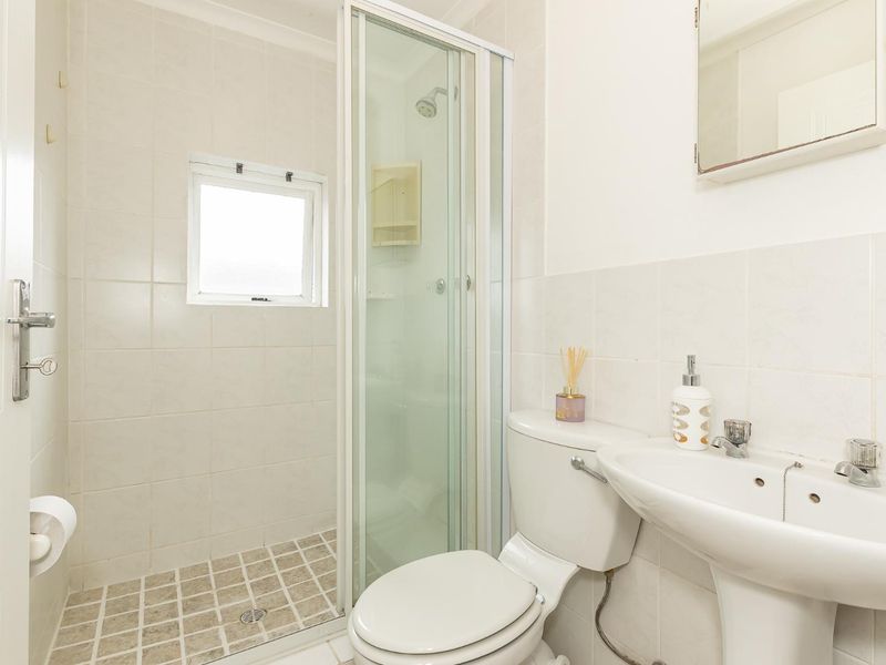 A functional bathroom featuring a shower enclosure, pedestal basin, toilet, and tiled finishes, offering a clean and practical layout.