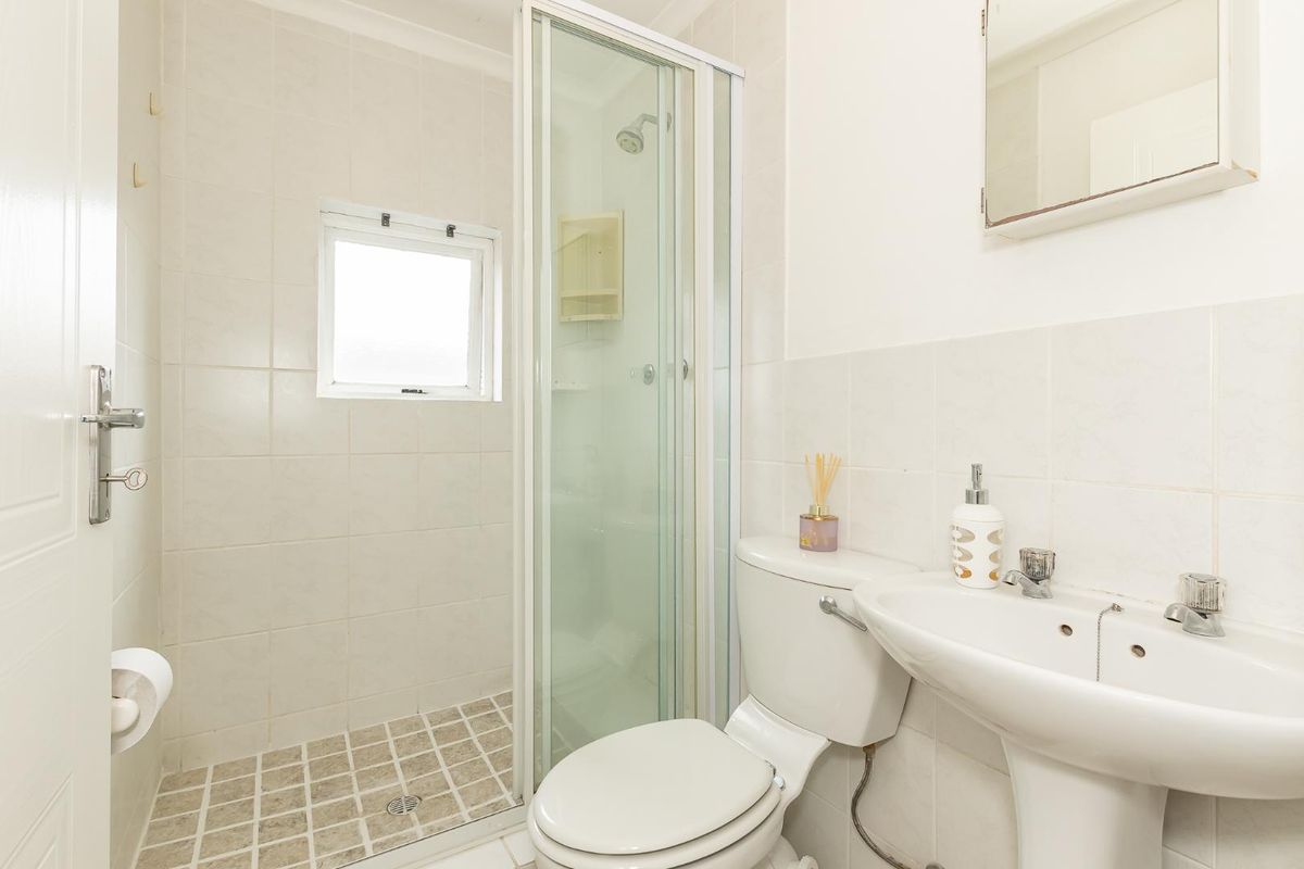 A functional bathroom featuring a shower enclosure, pedestal basin, toilet, and tiled finishes, offering a clean and practical layout.