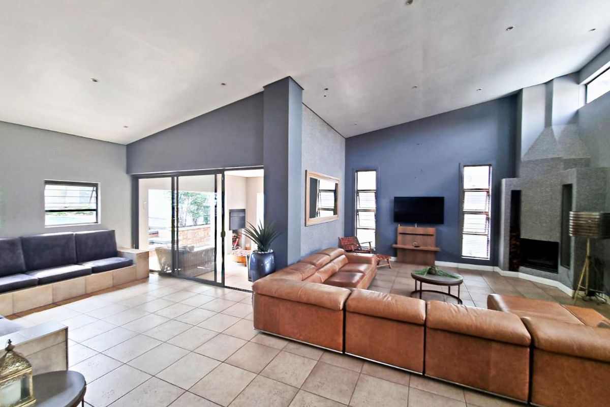 Spacious living room featuring a vaulted ceiling, tiled flooring, recessed lighting, and a prominent built-in fireplace with direct access to the patio.