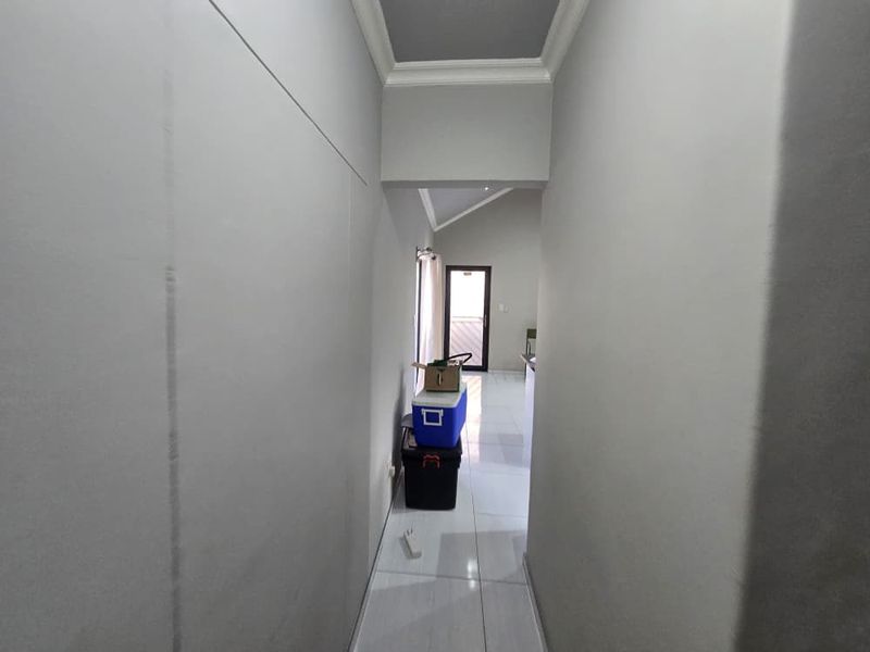 A clean, neutral-toned hallway featuring tiled flooring and coved ceiling details, providing a clear transition between living spaces.