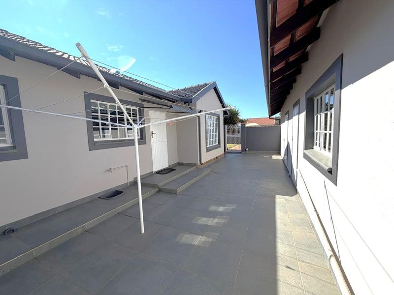 A clean and well-maintained paved rear courtyard area featuring tiled flooring, secure access gate, and exterior building finishes.