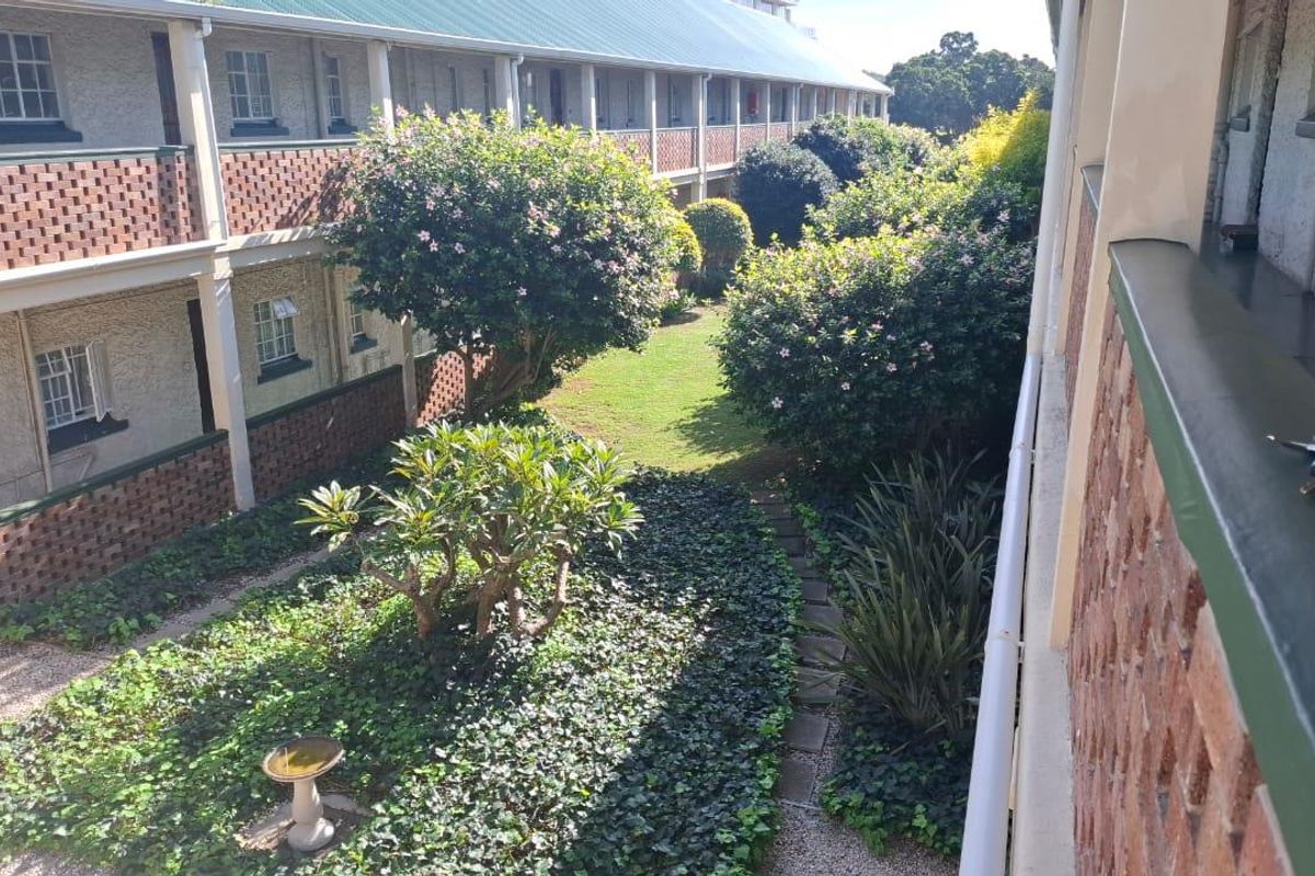 A view of the communal garden area and landscaped grounds situated between apartment building wings, featuring established greenery and paved pathways.