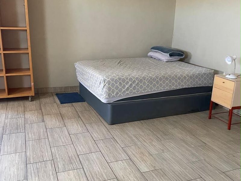 A bedroom featuring wood-look tiled flooring and an exposed steel beam ceiling structure, requiring cosmetic updates to improve the overall finish.