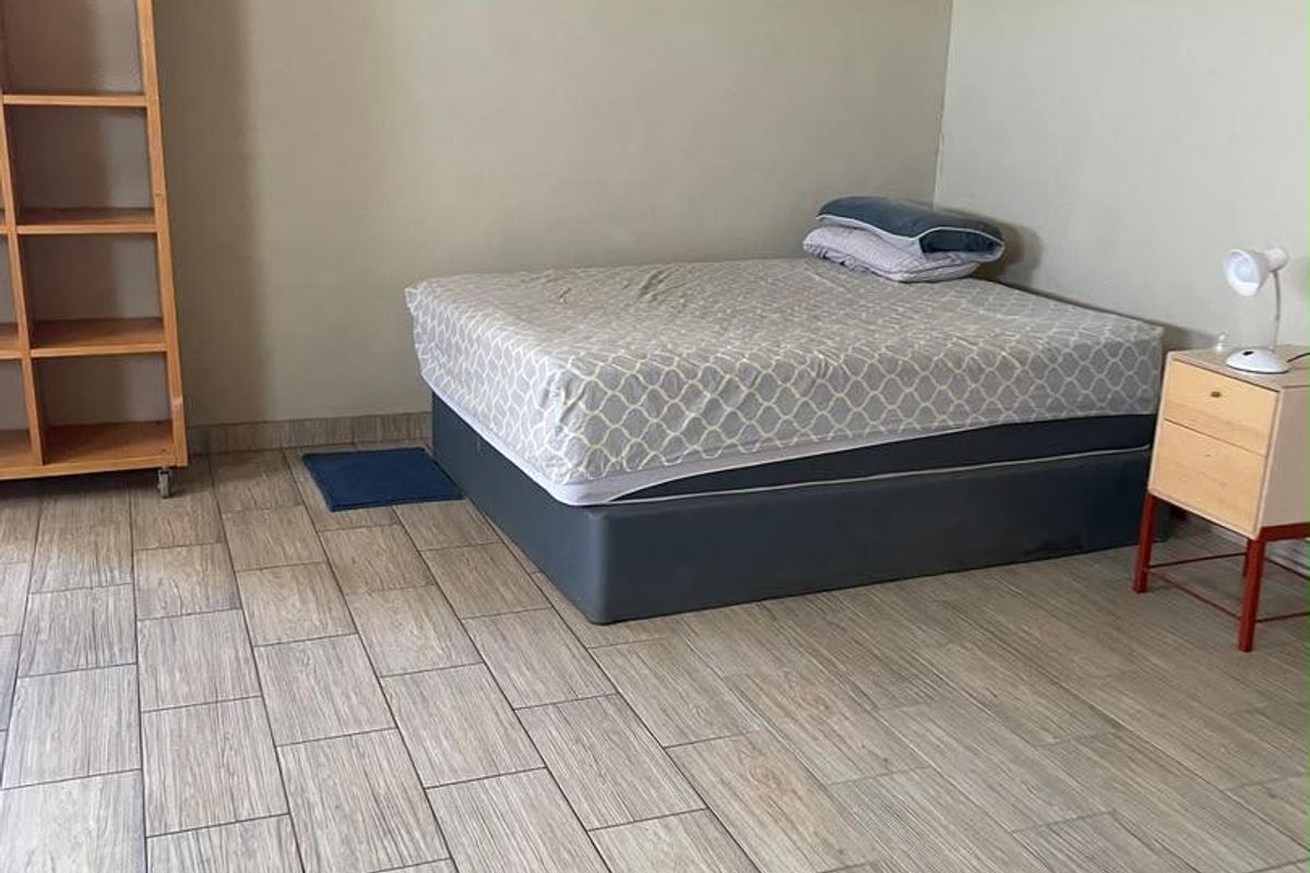 A bedroom featuring wood-look tiled flooring and an exposed steel beam ceiling structure, requiring cosmetic updates to improve the overall finish.