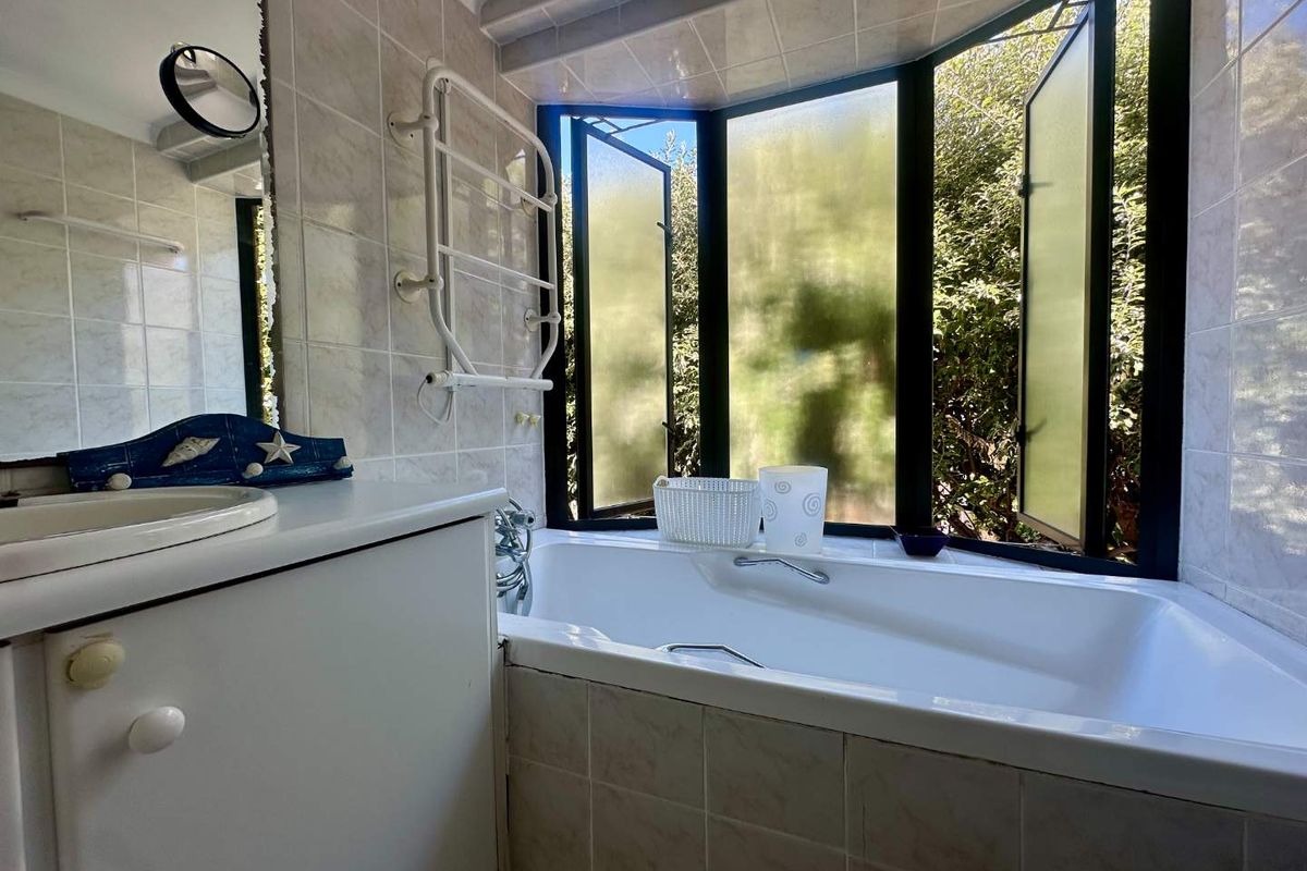 A functional bathroom featuring a built-in vanity, bathtub, and a heated towel rail, with large windows providing natural light and garden views.