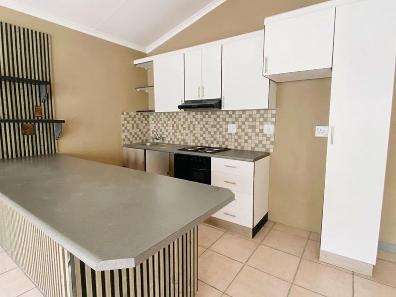 A functional kitchen featuring white cabinetry, a tiled backsplash, built-in oven and hob, and a breakfast bar with a neutral tiled floor.