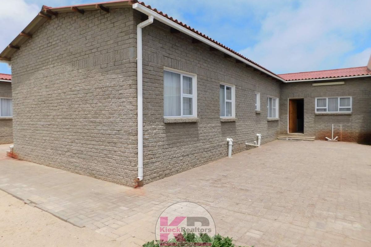 Rear exterior view of the property featuring exposed brick walls, a paved courtyard area, and a tiled roof with integrated guttering.