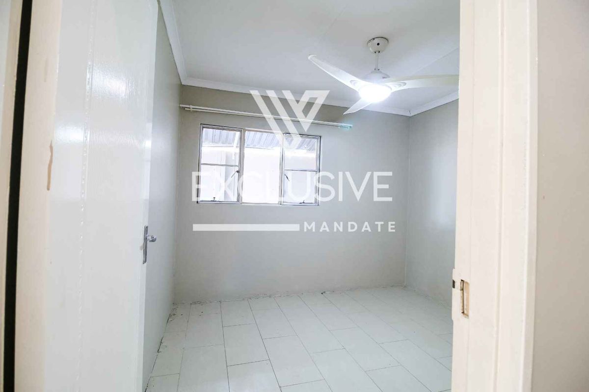 A simple, empty bedroom featuring tiled flooring, a ceiling fan, and a window providing natural light.