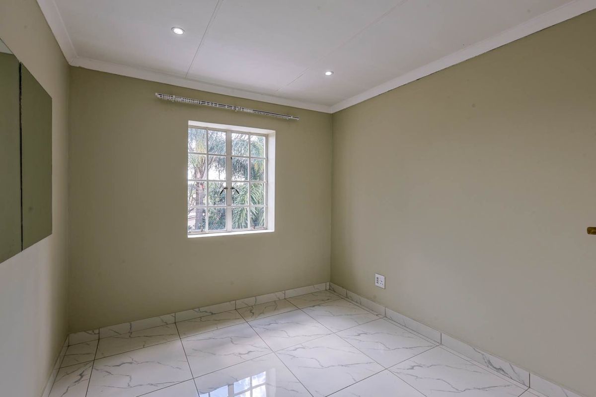 A bright, empty bedroom featuring modern white marble-look floor tiles, neutral wall paint, and a window with security bars.