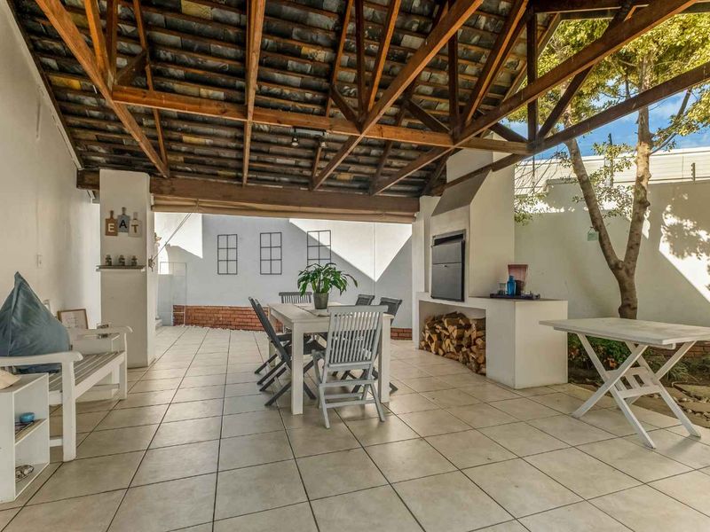 Covered outdoor patio featuring exposed timber roof trusses, tiled flooring, and a built-in braai area, perfect for alfresco dining and entertaining.