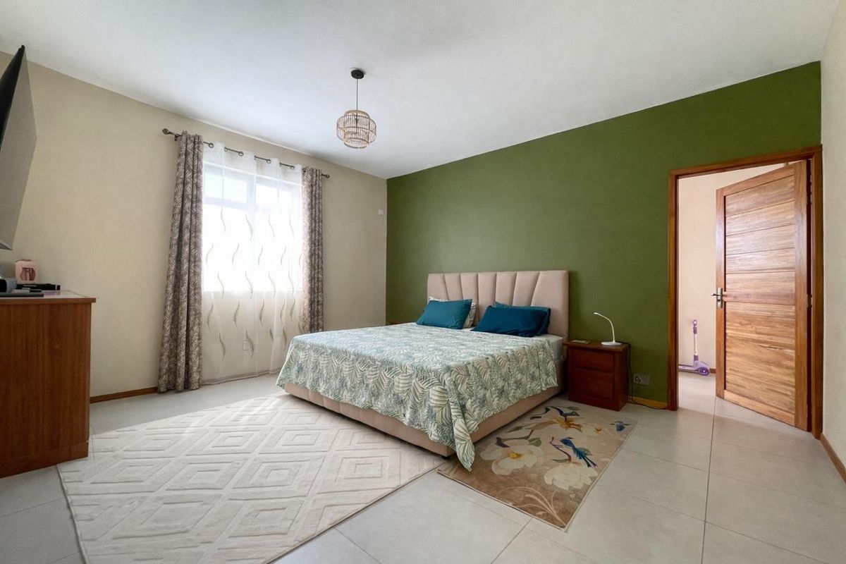 A spacious bedroom featuring tiled flooring, a green accent wall, and a wooden door leading to an adjacent room.