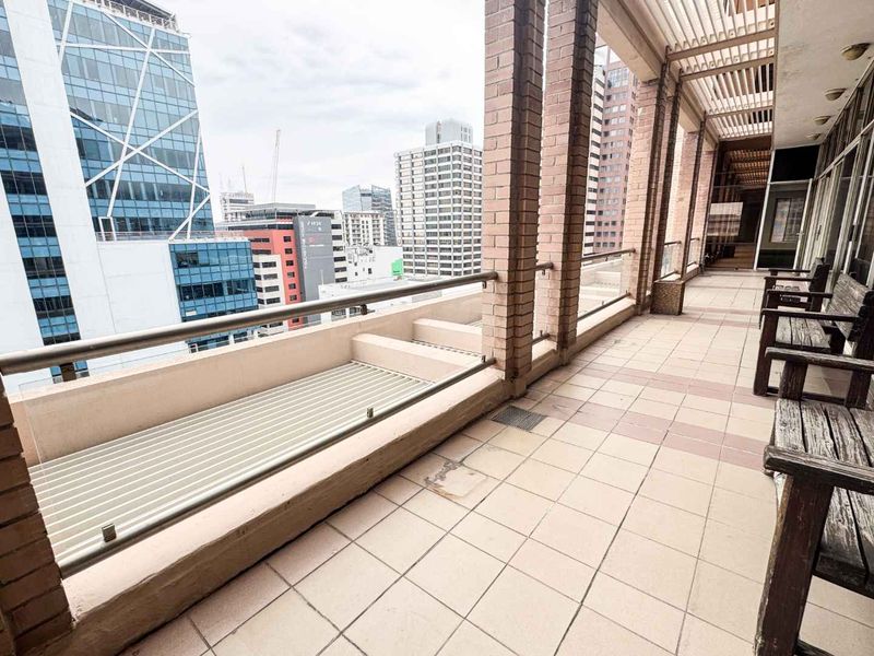 Spacious covered balcony featuring brick pillars, tiled flooring, and expansive city views, providing an ideal outdoor space for office staff.
