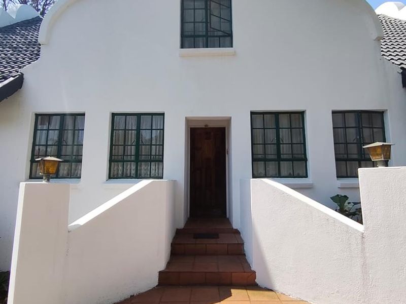 Front elevation of a Cape Dutch style house featuring a distinctive gabled roofline, tiled entrance steps, and dark timber front door.