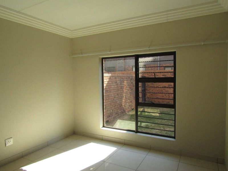 A clean, empty bedroom featuring neutral tiled flooring, cornice detailing, and an aluminium window with security bars overlooking a private rear courtyard.