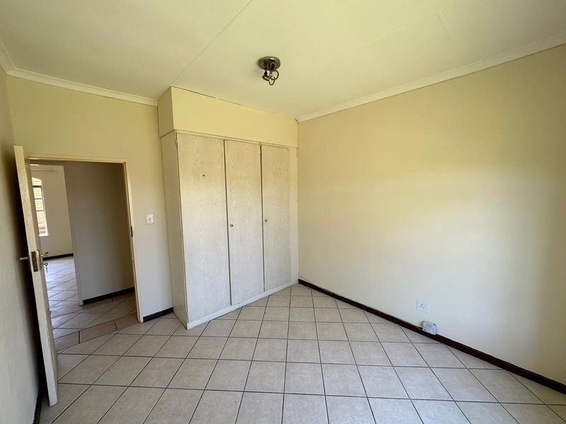 An empty bedroom featuring tiled flooring, built-in cupboards, and neutral wall finishes, offering a blank canvas for personalization.