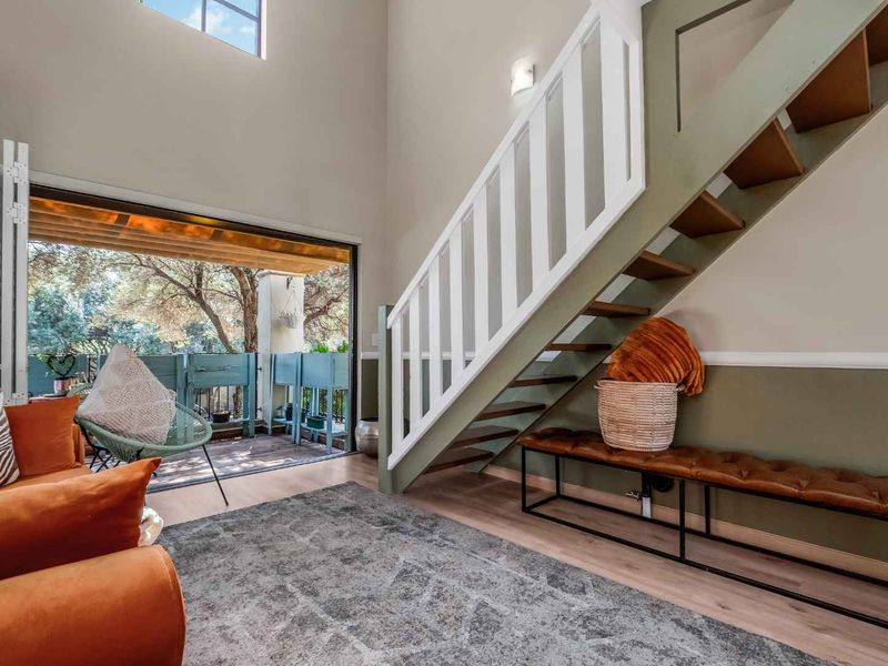 Bright living area featuring a staircase with white railing, high ceilings, and large sliding glass doors opening onto a private balcony.