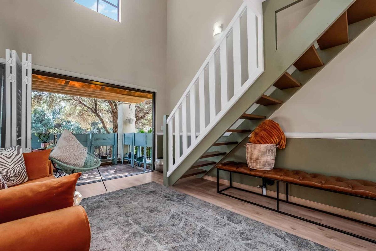 Bright living area featuring a staircase with white railing, high ceilings, and large sliding glass doors opening onto a private balcony.