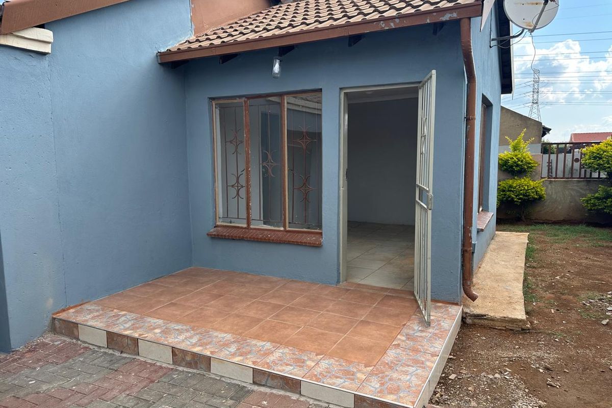 Exterior view of a house featuring a tiled patio, security gate, and metal-framed windows with security bars.
