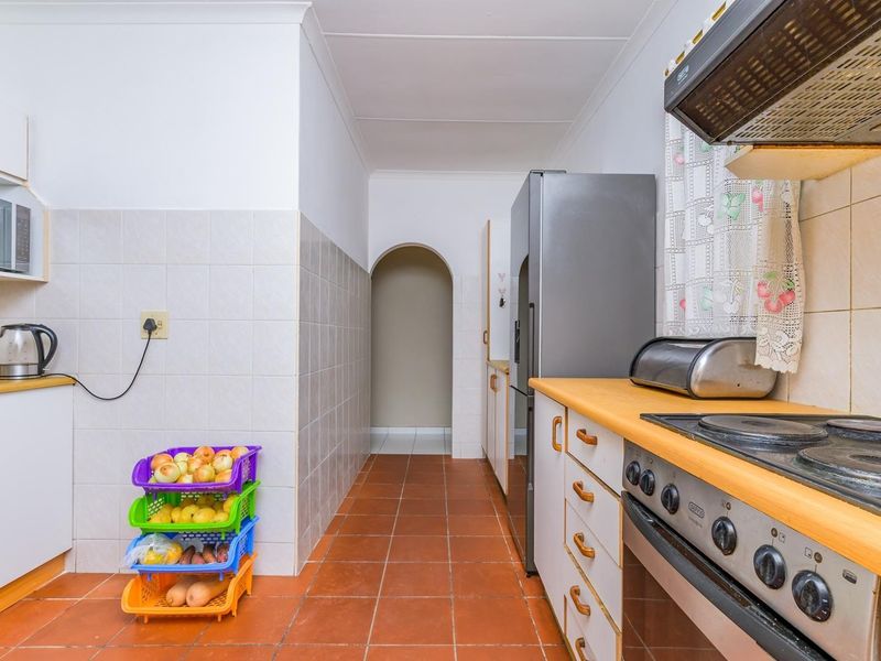 A functional kitchen featuring tiled flooring, built-in cabinetry, an electric hob with extractor fan, and a convenient archway leading to adjacent living spaces.