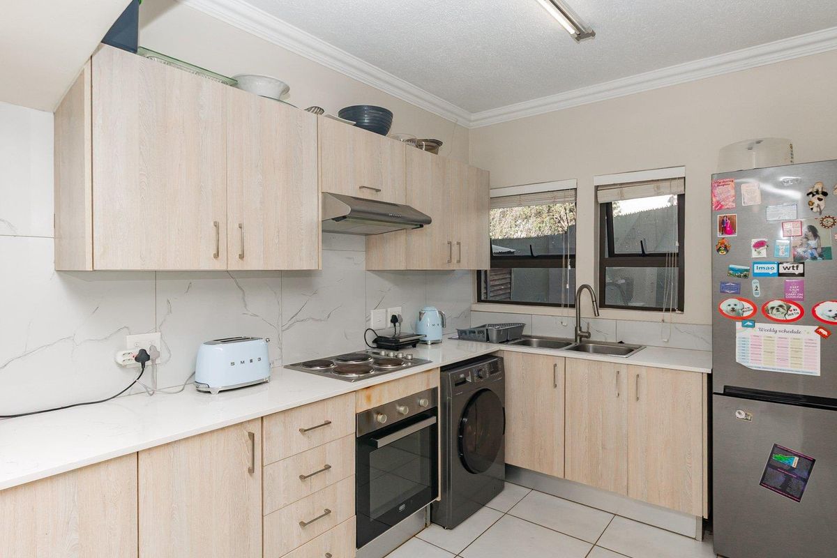 A functional kitchen featuring light-wood cabinetry, marble-look backsplash, built-in oven, electric hob, and a stainless steel double sink with tiled flooring.