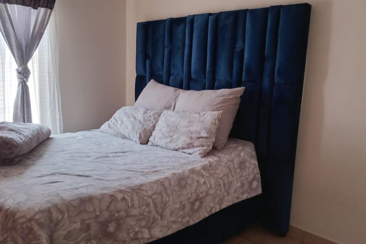 A bedroom featuring a tall, blue upholstered headboard and neutral wall finishes, providing a comfortable and functional sleeping space.