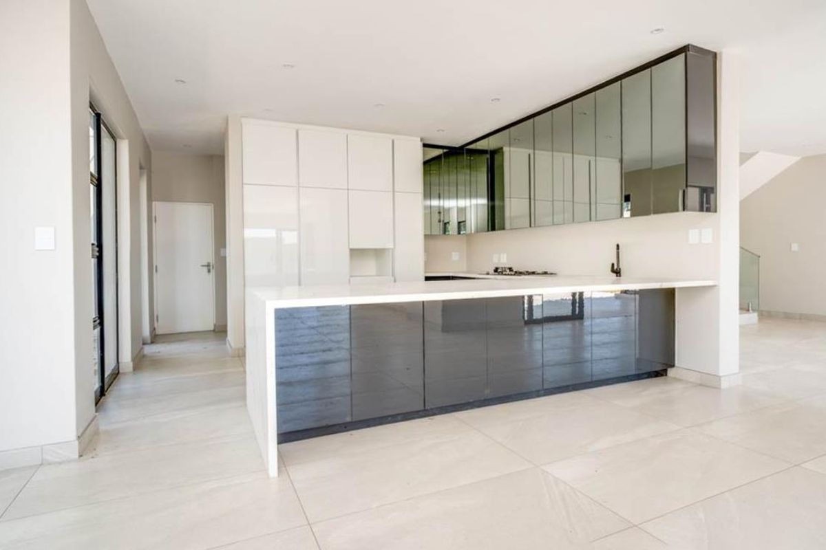 Modern open-plan kitchen featuring high-gloss cabinetry, a large waterfall-edge island, integrated cooktop, and sleek mirrored upper cabinets.