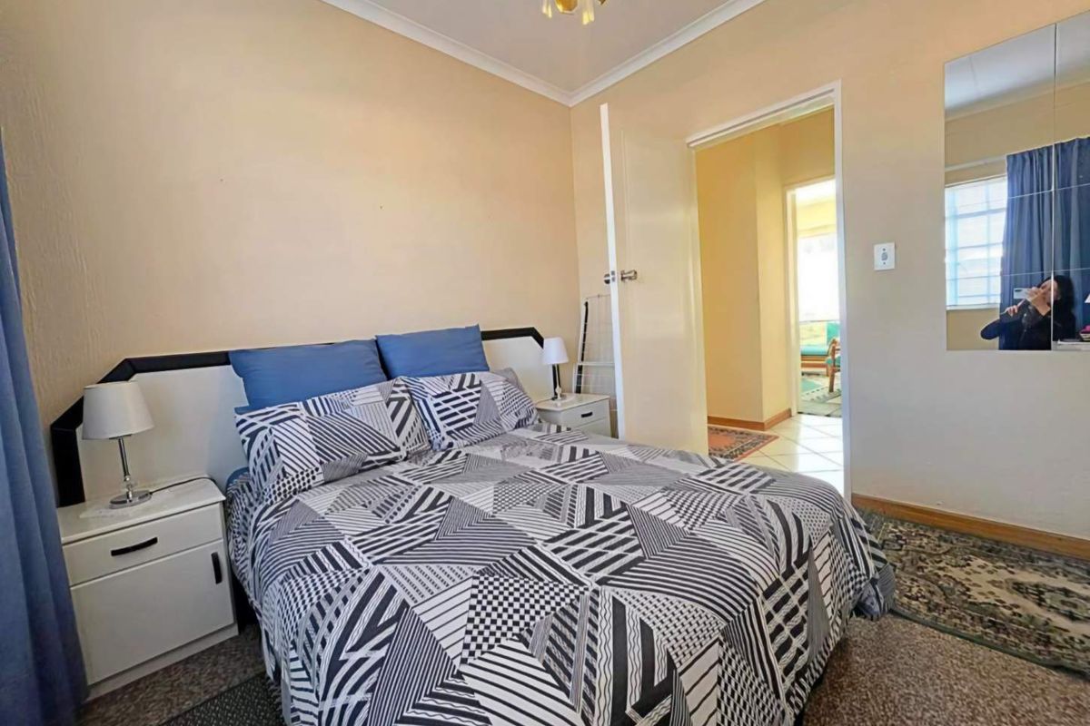 A bedroom featuring neutral wall tones, carpeted flooring, and a doorway leading to an adjacent living space.