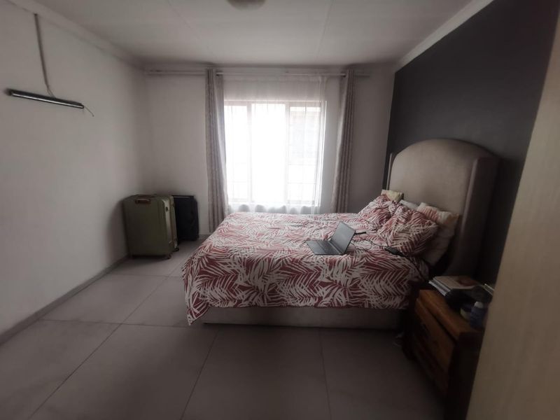 A bedroom featuring tiled flooring and a dark accent wall, with a window providing natural light.