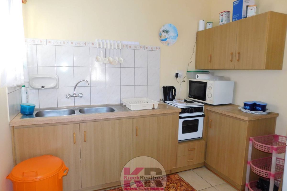 A functional kitchen featuring light wood-look cabinetry, a double stainless steel sink, tiled splashback, and a built-in oven with hob.