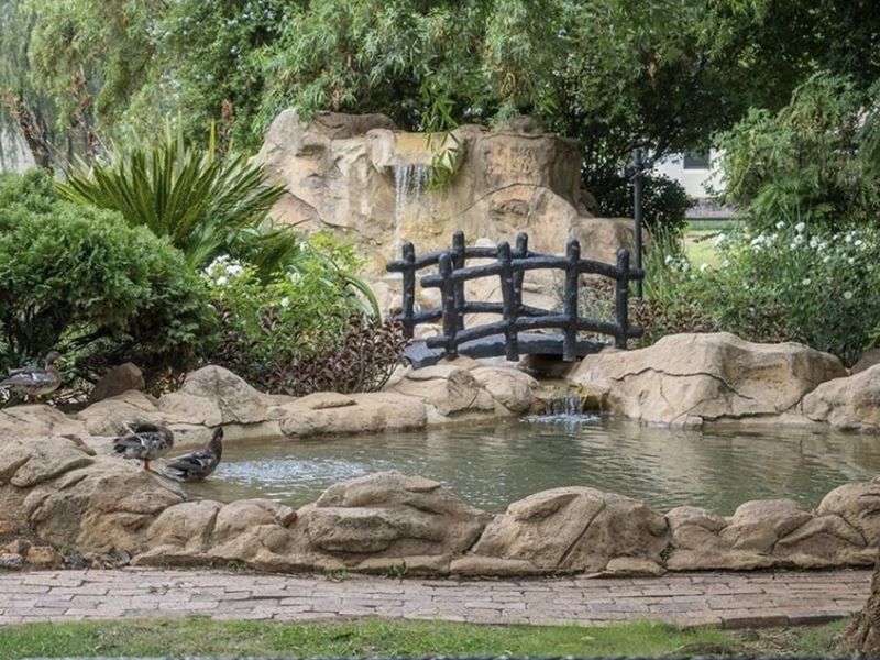 A beautifully landscaped garden area featuring a stone-lined pond, a small waterfall, and a decorative bridge, creating a serene outdoor environment.